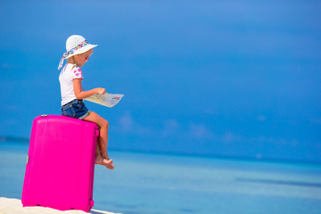 Fototapeta premium Little adorable girl with big pink suitcase and map of island on white beach