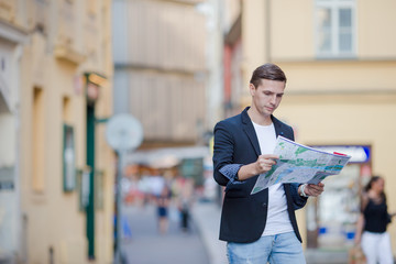 Young man in sunglasses with a city map and backpack in Europe. Caucasian tourist looking at the map of European city in search of attractions.