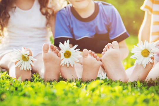 Kids feet with daisy flower on green grass in a summer park.