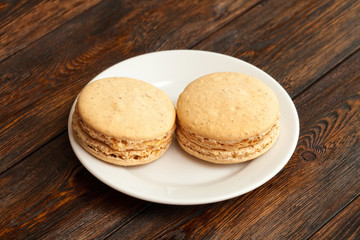 Two traditional french chocolate macarons on plate, wooden background