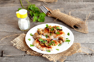 Roasted Turkey breast steaks with cheese and mushrooms on a plate. Salt shaker, fork, knife, fresh raw parsley on an old rustic table. Cooking Turkey meat