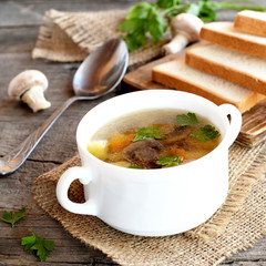 Diet mushroom soup with vegetables, sliced white bread on a kitchen cutting board, spoon, parsley, fresh agaricus on a wooden table. Lenten mushroom soup in a bowl and on a burlap. Closeup