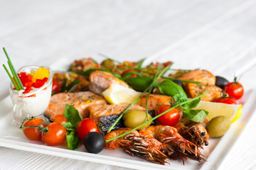Grilled assorted seafood with sauce, blurred background with copyspace for text, focus on roasted shrimps with tomatoes and olives