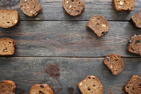 Sweet rye bread on dark wooden background, copyspace. Dark bruschetta slices with hazelnuts and raisins frame on old rustic table, flat lay, frame