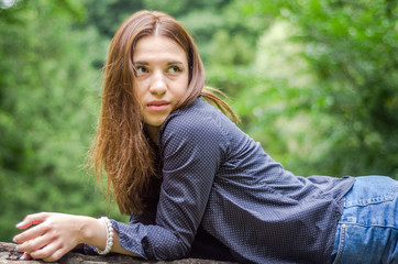 Naklejka na ściany i meble Young beautiful teenager girl with long hair in a shirt and denim shorts resting on a tree during a walk in the park Striysky in Lviv hot sunny summer day among the bushes and trees leaves