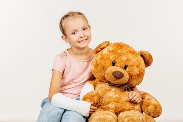 Young girl with broken arm is holding a soft toy bear. Concept o
