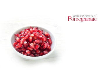 seeds of pomegranate in a small bowl on white painted wood, sample text