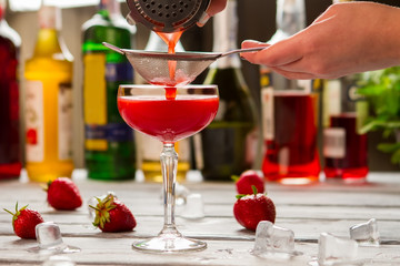 Red beverage pours through sieve. Male hand holding a sieve. Bartender's recipe of clover club. Fresh summer drink.