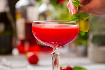 Glass with red drink. Man's hand holding mint sprig. Clover club with fruit syrup. Egg white and lemon juice.