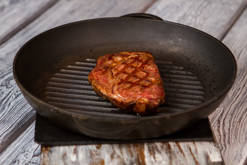 Piece of meat on pan. Frying pan on wooden background. Preparation of ribeye steak. Juicy beef cooked at restaurant.