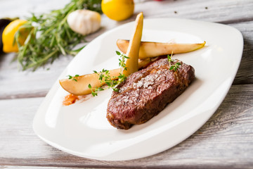 Brown meat on white plate. Salt and green herb. Ribey steak with sweet pear. Meat dish with barbecue sauce.