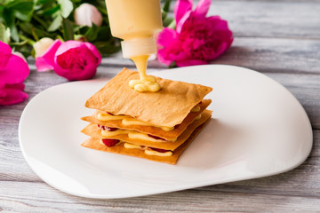 Bottle puts custard on shortcake. Pastry on white plate. Fresh and sweet filling. Preparation of dessert at cafe.