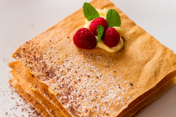Pastry with raspberries. Small leaves of mint. How to prepare millefeuille. Powdered sugar and chocolate crumbs.