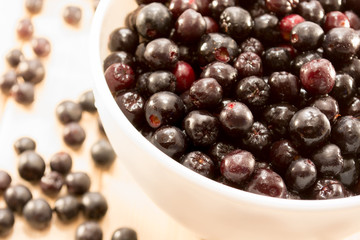 Bowl full of aronia spilled on wooden table