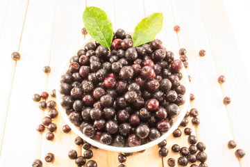 Bowl full of aronia spilled on wooden table