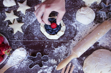 Women hands cook home-made dough cake with a stuffing from ripe strawberry and juicy berries of a honeysuckle. Food concept on a wooden dark table. Top view. House pastries background