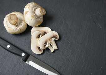 Sliced mushrooms with a sharp knife on a slate chopping board background