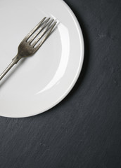 A silver fork and white plate on a rustic slate background