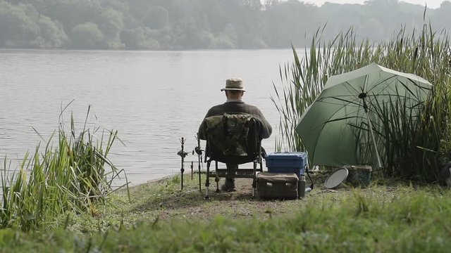 A pensioner is enjoying a day fishing in a beautiful idyllic fishing spot on the edge of a peaceful lake.