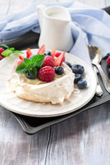 Meringues Pavlova cake with fresh raspberry and blueberry on a white rustic wooden background, selective focus
