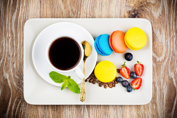 Cup of coffee with macaroons and berries on wooden background