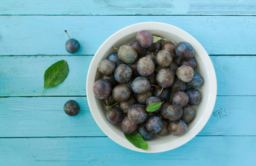 Fresh ripe plums in bowl on blue wood background