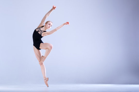 Fototapeta Ballet Perfection. Young and beautiful ballerina in a black dancing suit is posing in a white studio full of light.
