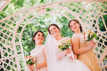 Beautiful brunette bride and gorgeous bridesmaids with bouquets posing near stairs