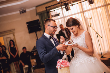 Bride and Groom at Wedding Reception Cutting the Wedding Cake. They feed each other cake. Wedding restaurant. 