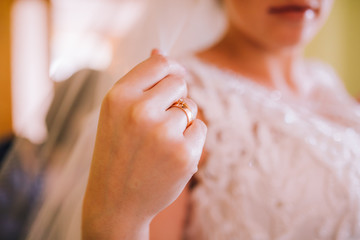Beautiful brunet bride in white wedding dress standing at her bedroom near the window. Morning bride preparation.