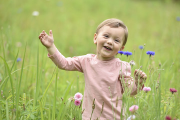 Cute 2-year-old girl playing in wild flower field