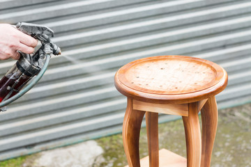Carpenter is covering stool by lacquer. Furniture varnishing using sprayer or pulverizer