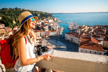Young female traveler with red backpack and hat enjoying the view from George's tower on Piran old...