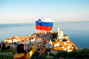 Young woman waving slovenian flag on Piran coastal town background. Promoting tourism in Slovenia