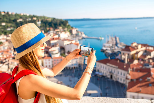 Young female traveler with red backpack and photo camera enjoying the view on Piran old town. Traveling in Slovenia