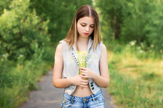 Female teenager dressed in stylish denim vest and jeans holding daisy flowers