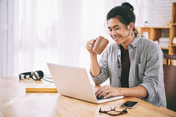 Joyful Asian man drinking coffee and browsing internet
