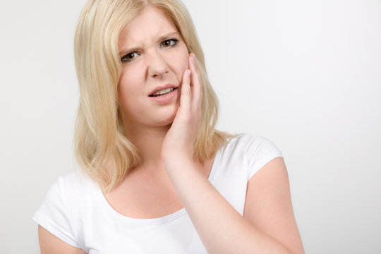 Junge Frau hält sich Wange vor Zahnschmerzen