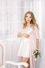 Obraz premium Attractive young blonde pregnant woman posing in white nightgown. Happy glamour sexy girl at home.