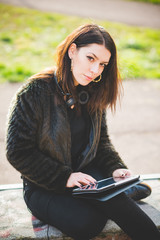 Young beautiful caucasian indie woman with septum piercing using tablet outdoor in city back light, looking at camera smiling - serene, technology, social network concept