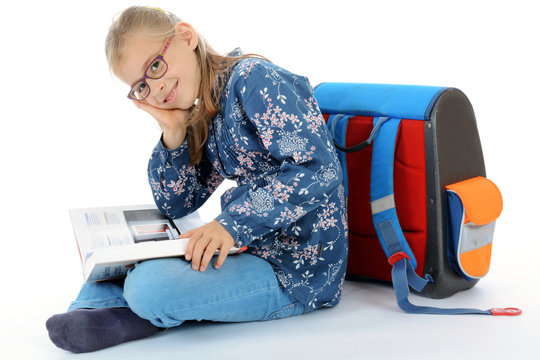 Schulkind mit Tornister liest Buch als Hausaufgabe f&uuml;r Grundschule