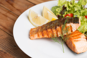 Grill salmon steak serve with lemon and colorful salad on wooden table