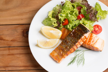 Grill salmon steak serve with lemon and colorful salad on wooden table