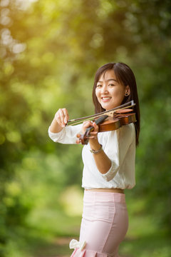 asia woman playing violin in garden with sunshine
