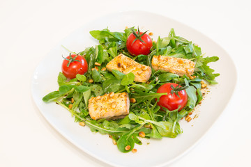 Salad with grilled salmon, green salad and pine nuts on a white plate