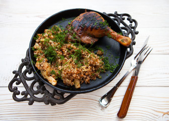 Chicken grilling with a side dish of buckwheat, on a black metal