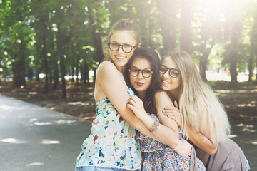Three beautiful young boho chic stylish girls walking in park.