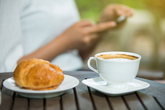  woman drinking coffee and usr smartphone in the garden