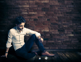 High school boy sitting inside old room squeezing paper and throwing it on floor