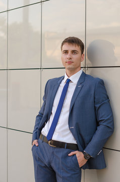 Portrait of a young successful man economist standing in modern office interior, confident male dressed in luxury corporate clothes using digital tablet during work break.